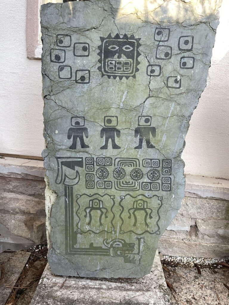 Alien Monolith #4 by Bruce Bennett, a carved stone sculpture with stylized figures and geometric motifs