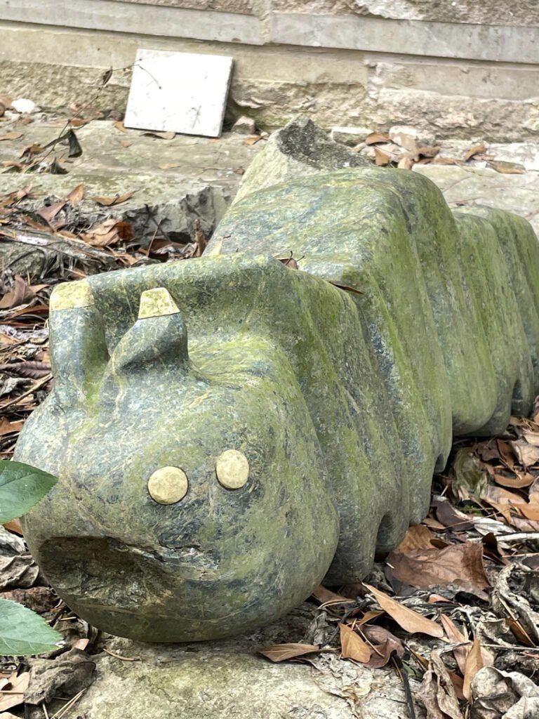Mum Caterpillar by Bruce Bennett, a segmented stone caterpillar sculpture with round eyes and short antennae in the Spring Creek garden