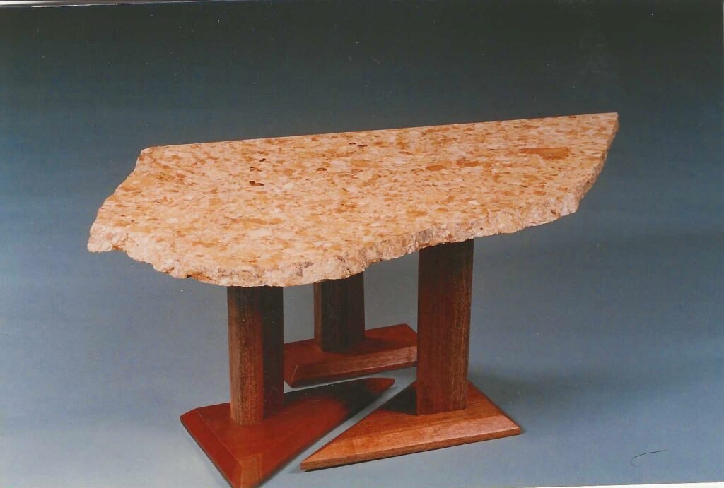 Bruce Bennett dining table featuring a natural-edge Giallo granite top supported by a geometric wood base.