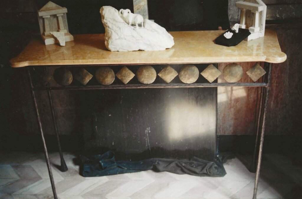 Bruce Bennett console table with a polished stone top, metal base, and alternating carved stone circles and diamonds, displayed with several of Bennett’s small sculptures.