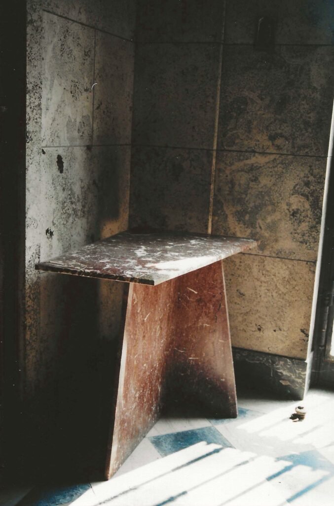 Rosso Levanto marble table by Bruce Bennett with a rectangular stone top and angled pedestal base.