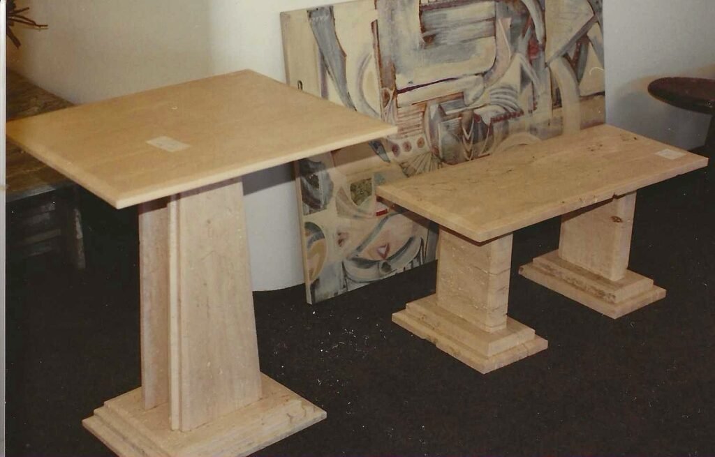 Bruce Bennett tables in Italian Cream marble featuring geometric tops and architectural pedestal bases.