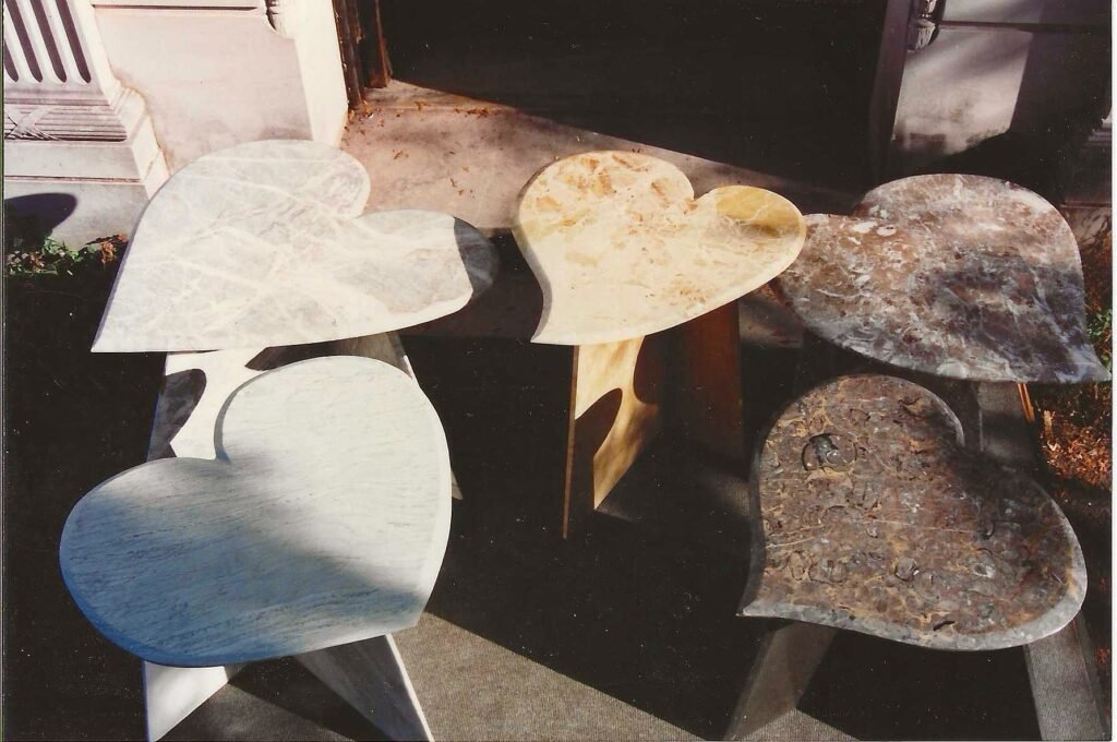 Group of Bruce Bennett heart-shaped stone tables in varied marble and granite, featuring contrasting sculptural bases.