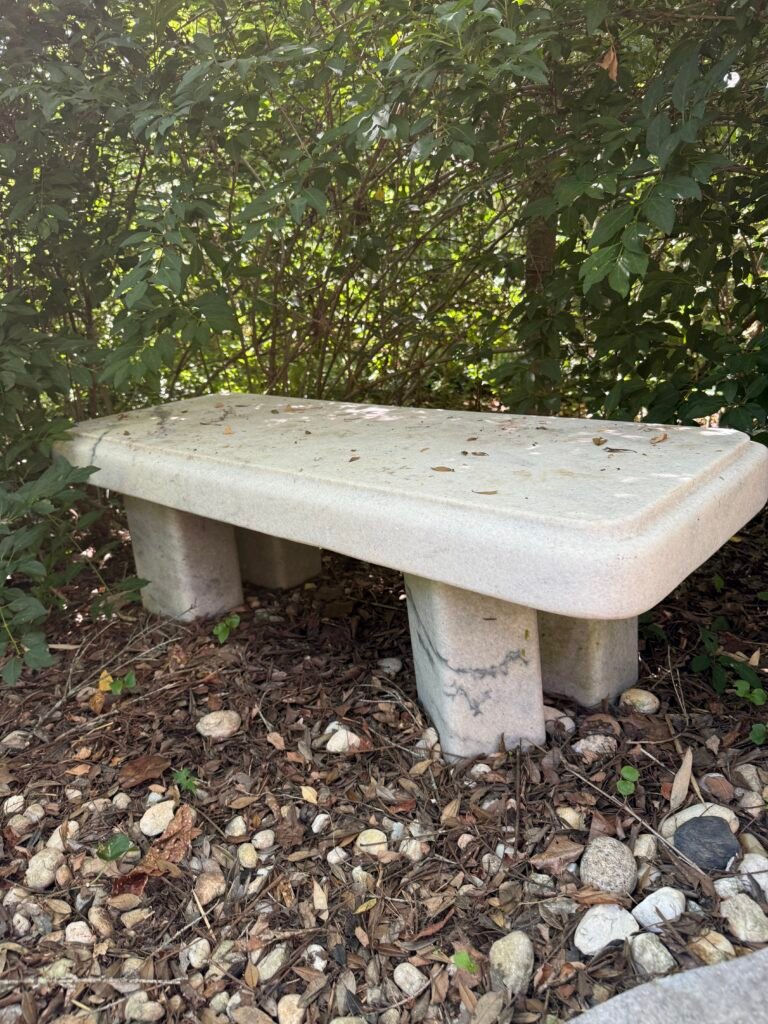 Carrara marble bench by sculptor Bruce Bennett with a thick rectangular seat, rounded edges, and stone supports.
