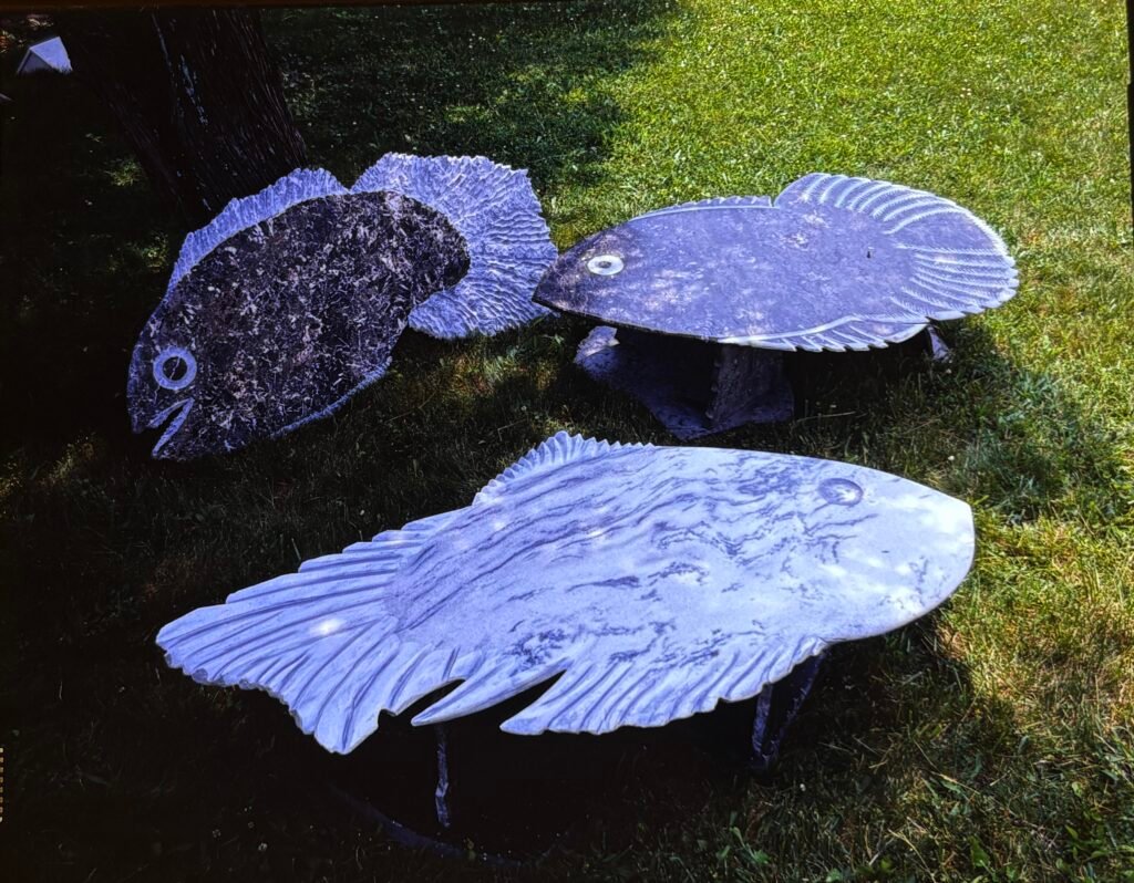 Three fish-shaped sculptural granite tables by Bruce Bennett, featuring carved fins, tails, eyes, and natural stone patterning.