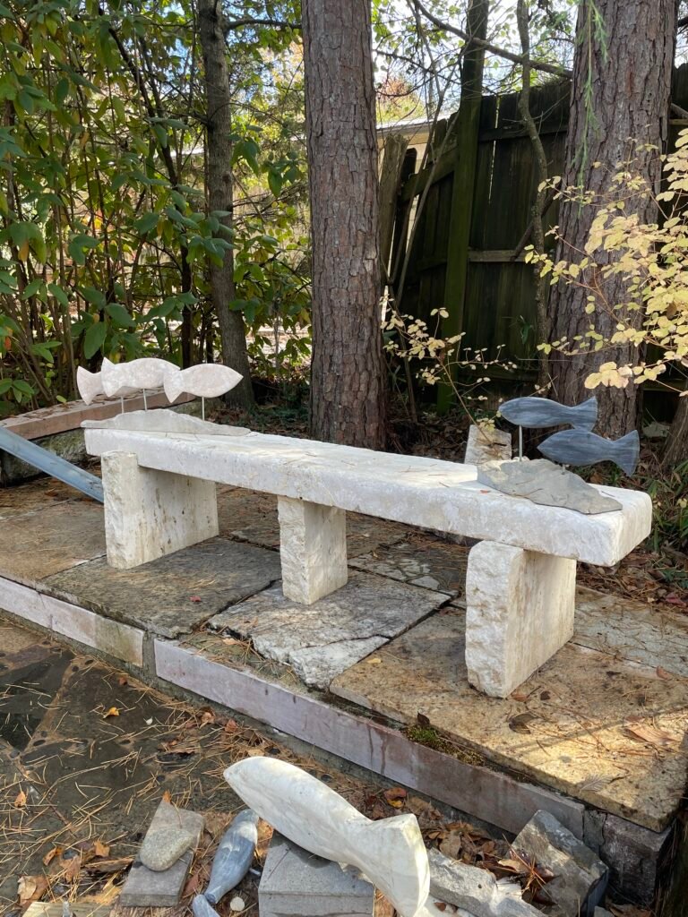 Travertine marble bench by sculptor Bruce Bennett with a thick stone seat, rough natural edge, and rectangular stone supports.