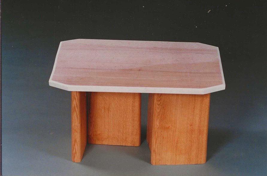 Wood table by Bruce Bennett with a broad rectangular top with clipped corners and three curved wooden supports.